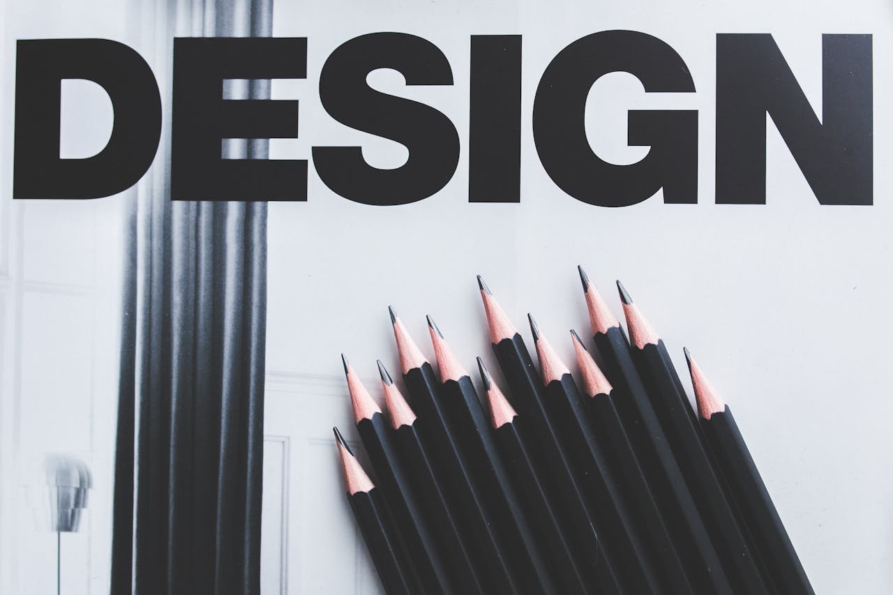Black pencils arranged creatively next to large typography 'DESIGN'.